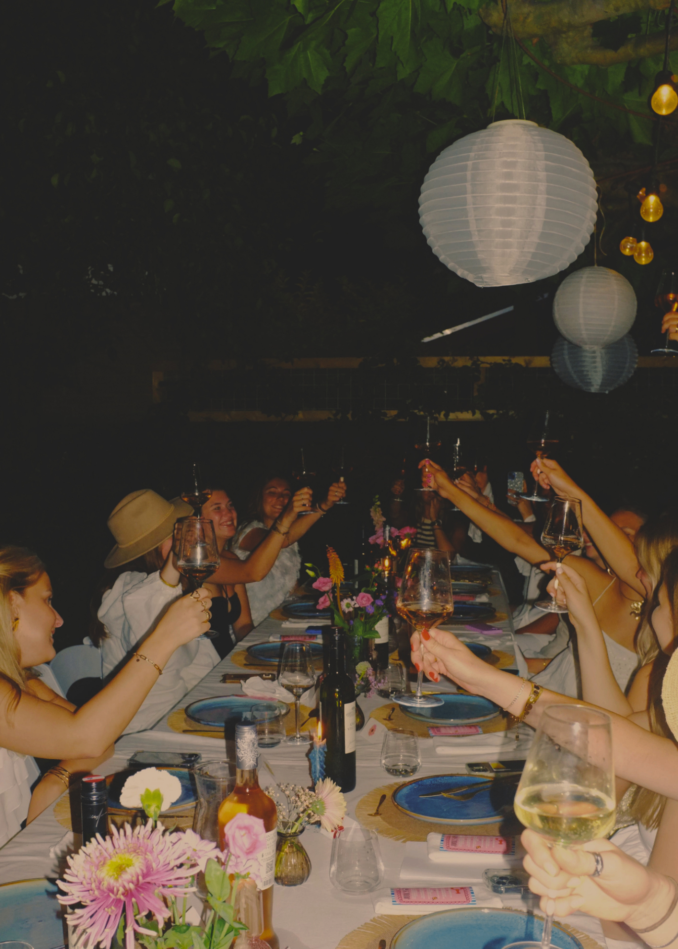 Women raising glasses in a toast around a candlelit dinner table at night